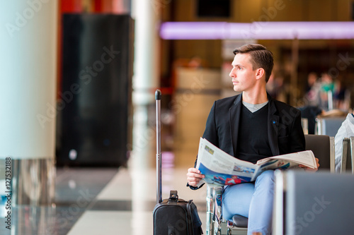 Young caucasian man with newspaper at the airport while waiting for boarding. Casual young businessman wearing suit jacket.