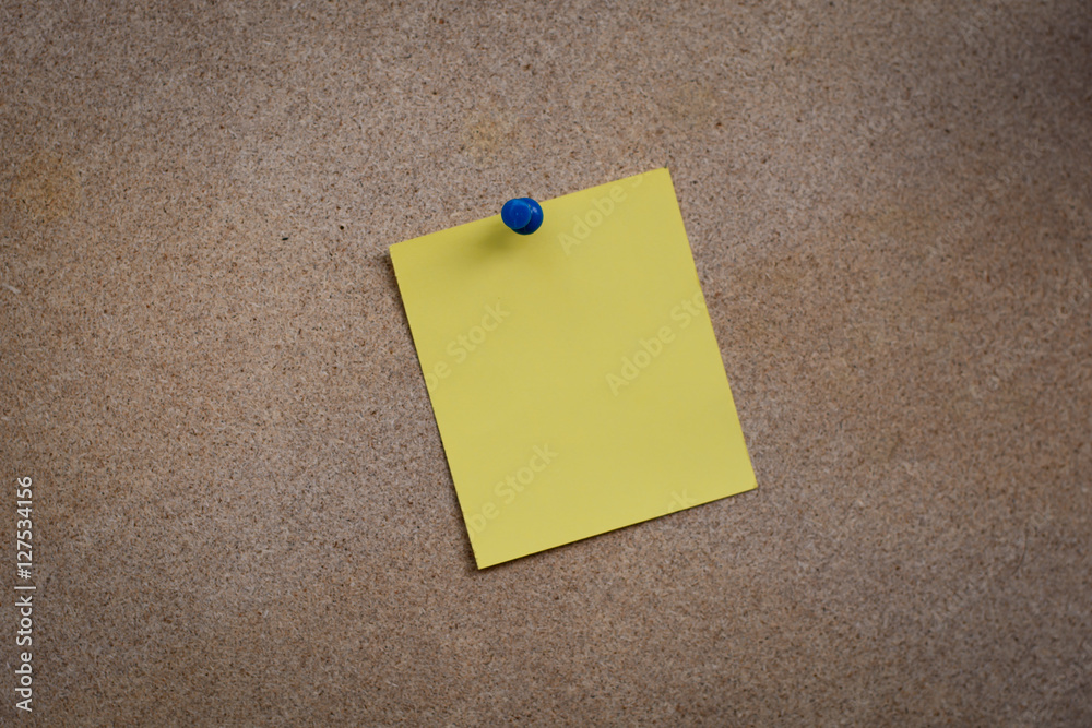 Blank yellow paper note pinned on cork board with white thumbtac Blank yellow paper note pinned on cork board with white thumbtac