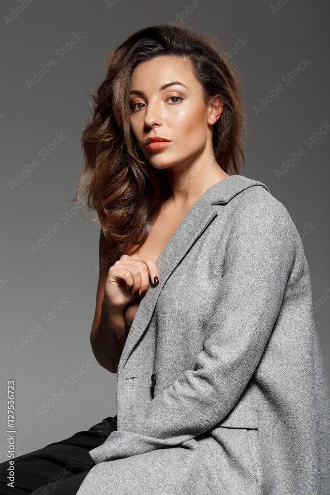 Young beautiful woman looking at camera sitting over grey background. Young beautiful woman looking at camera sitting over grey background.