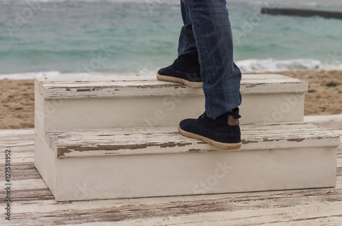 Man's foot walking up on wooden ladder. Sea on background