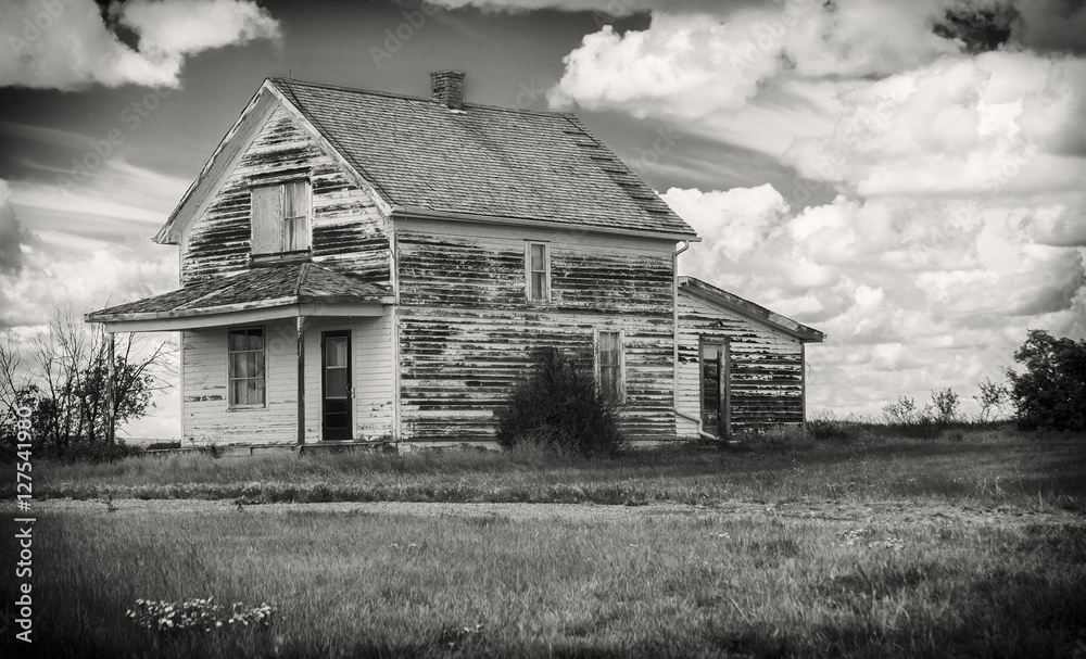 horizontal black and white image of an old rustic abandoned house with a veranda sitting under a cloudy sky. horizontal black and white image of an old rustic abandoned house with a veranda sitting under a cloudy sky.