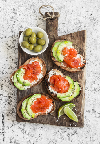 Delicious appetizers with wine - cream cheese, smoked salmon and avocado sandwiches and olives on a wooden board. On a light background, top view