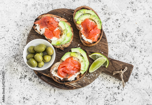 Delicious appetizers with wine - cream cheese, smoked salmon and avocado sandwiches and olives on a wooden board. On a light background, top view