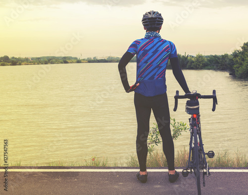 Young man with bicycle standing on the nearby lake in holiday mo