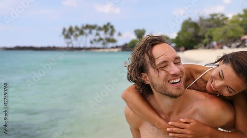 Attractive happy couple laughing having fun piggybacking on tropical beach. Caucasian man carrying Asian girlfriend having fun laughing on travel vacation. Healthy happy interracial people. 59.94 FPS. photo