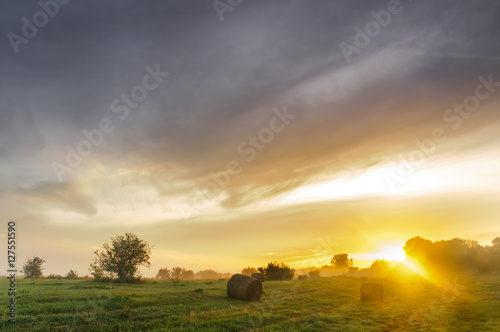 Sunrise over a misty meadow with straw blocks