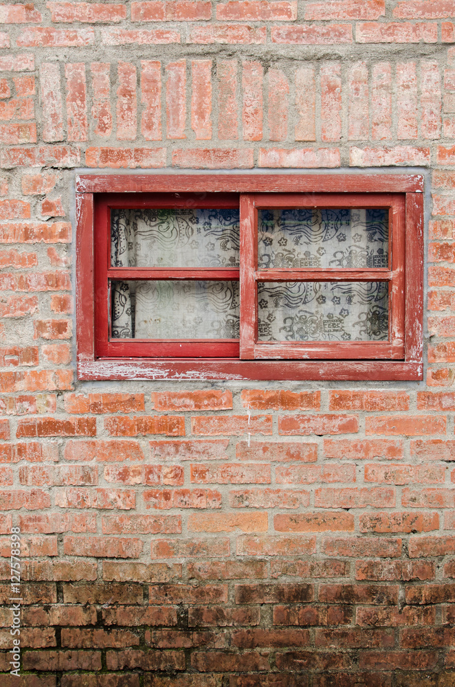 Old window with red wooden frames on brick wall. Curtain drawn down inside the window.