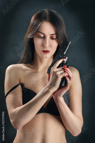 sad woman in lingerie with gun on black background