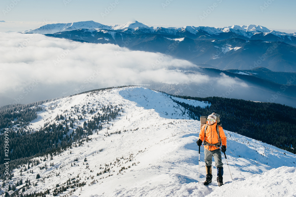 Man in bright clothes with a backpack climbs on top of snow-cove