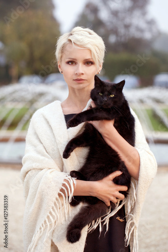 Obraz na płótnie a beautiful blonde woman with a black cat, holding a black cat, stroking a cat w salonie