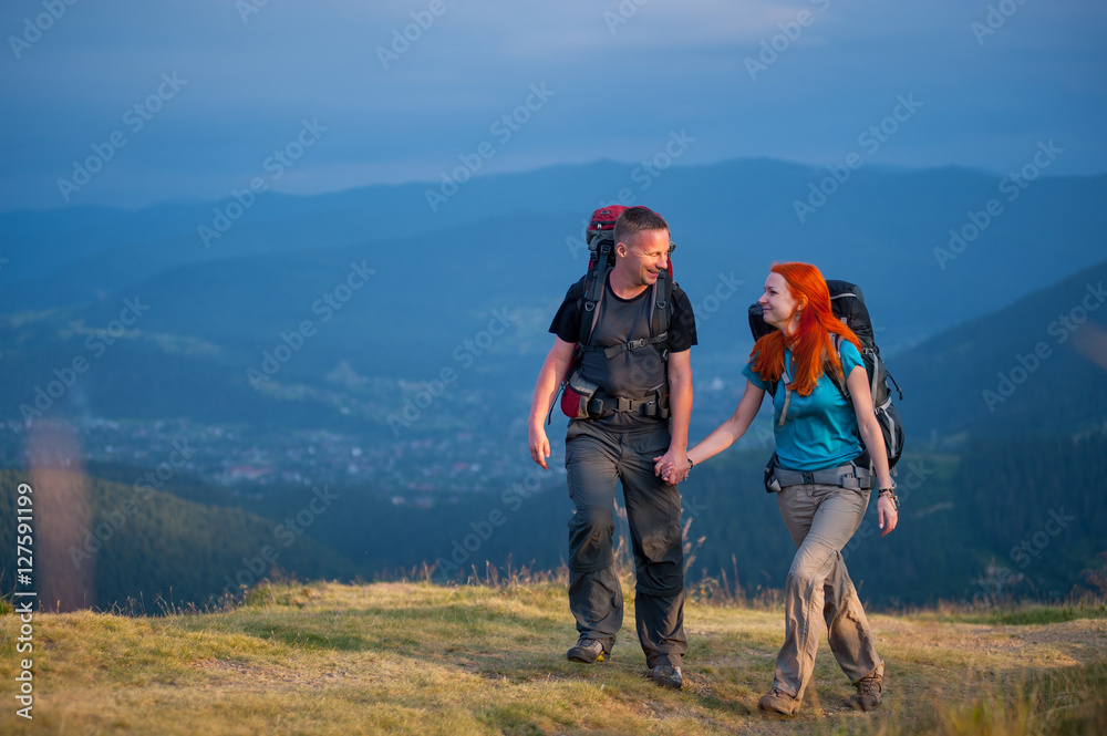 Young family of hikers with backpacks walking in the beautiful mountains area, holding hands and looking to each other. Lifestyle active vacations concept mountains landscape on background