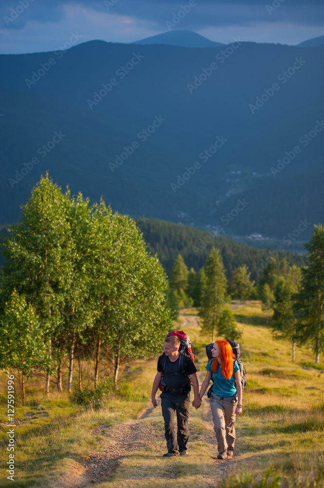 Tourists man and woman with backpacks walking along a beautiful mountain area, holding hands. Lifestyle active vacations concept mountains landscape on background