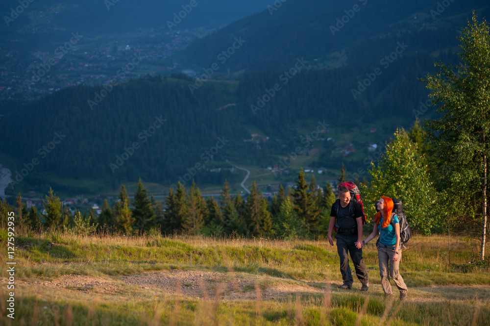 Couple of hikers with backpacks walking in the beautiful mountains area, holding hands and looking to each other. Lifestyle active vacations concept mountains landscape on background