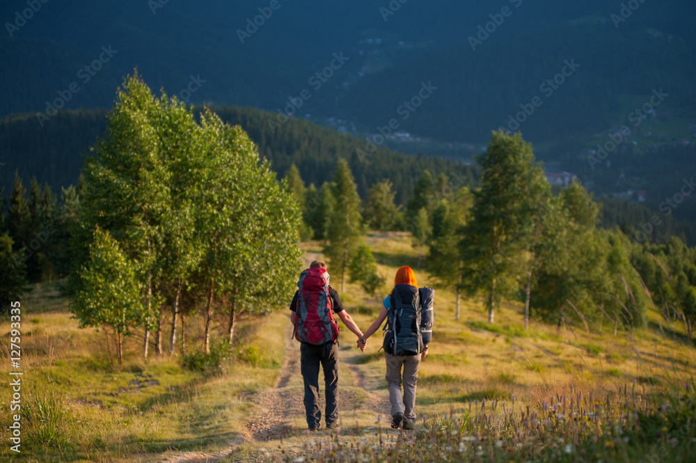 Back view couple hikers with backpacks walking along a beautiful mountain area and holding hands. Lifestyle active vacations concept mountains landscape on background