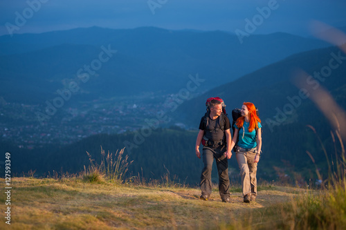 Tourists man and woman with backpacks walking in the beautiful mountains area, holding hands and looking to each other. Lifestyle active vacations concept mountains landscape on background © anatoliy_gleb