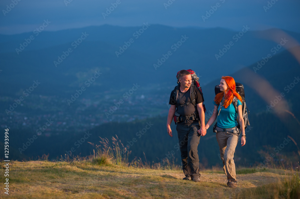 Happy couple of backpackers with backpacks hiking in the beautiful mountains area, holding hands and looking to each other. Lifestyle active vacations concept mountains landscape on background
