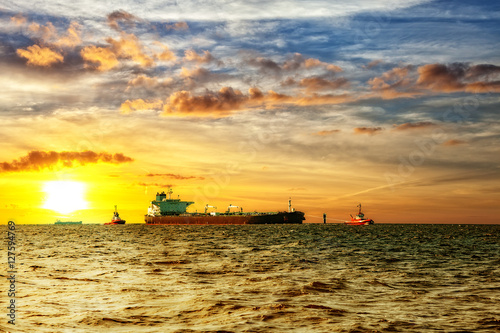 Tanker ship with escorting tugs on sea at sunrise.