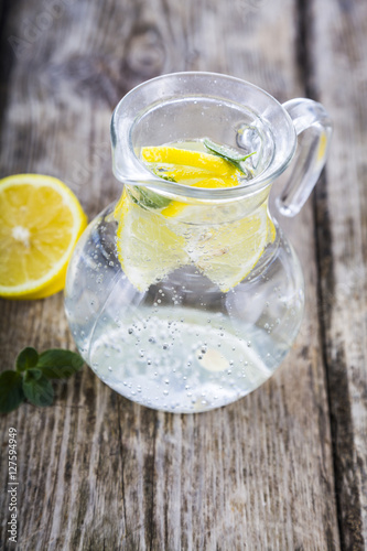 Homemade lemonade with lemons on a wooden table. Jug of cold wat