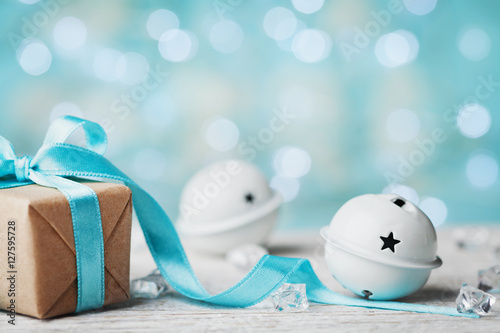 Christmas gift box and white jingle bell against turquoise bokeh background. Holiday greeting card. photo