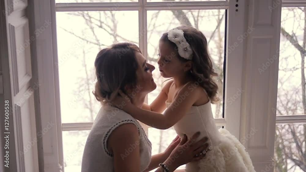 mother and daughter three years sitting by the large window in white dresses before the new year mother and daughter three years sitting by the large window in white dresses before the new year