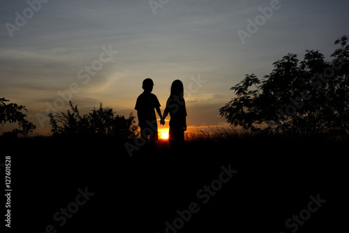Front view of a full body of couple silhouettes holding hands and walking together looking each other in a date at sunset.