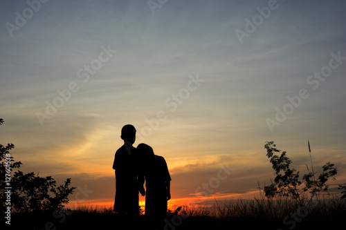 Front view of a full body of couple silhouettes holding hands and walking together looking each other in a date at sunset.