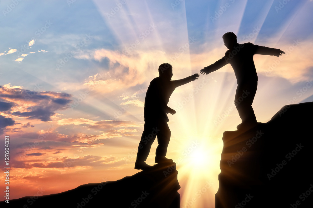 Man helps friend in mountains of giving helping hand sunset