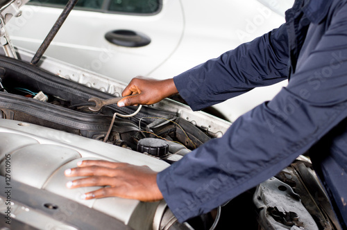 Close-up of a hand holding a key on the engine of a broken car.