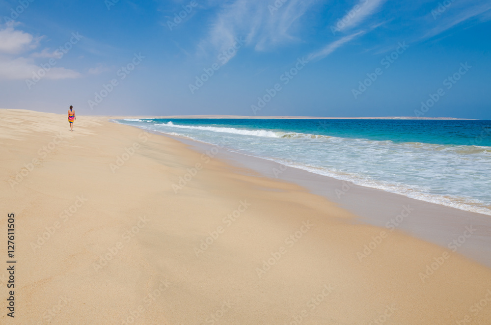 Lonely woman wearing colorful sarong walking along deserted beach