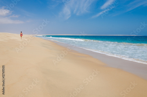 Lonely woman wearing colorful sarong walking along deserted beach