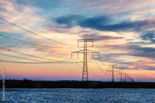 High voltage electricity lines over river at sunset