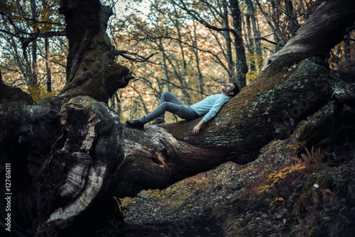 Joven vestido de azul descansando sobre la rama de un castaño centenario rota. Imagen bucólica.