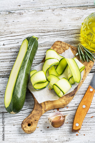 Thin slices of fresh zucchini on the cutting board  the olive tree  a simple wooden table with  bottle   oil for cooking homemade spring afternoon. The concept  home seasonal  natural food.