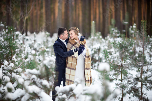 Winter wedding day, portrait of young bride and groom with plaid in the winter forest after wedding ceremony 