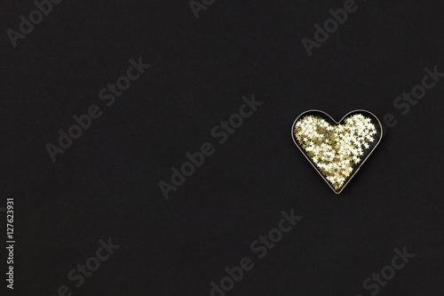 Small golden heart made of little stars on black background. Christmas concept