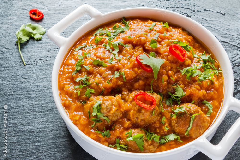 Spicy lentil and meatball soup with parsley. White casserole on black stone background.