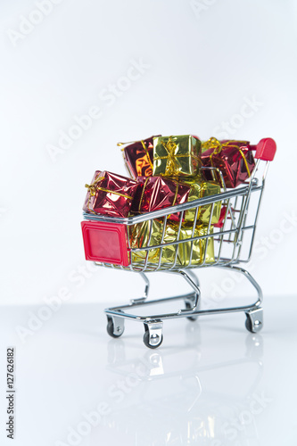 Christmas shopping background compostion of a multiple decoration balls and tiny shopping cart over the wooden surface