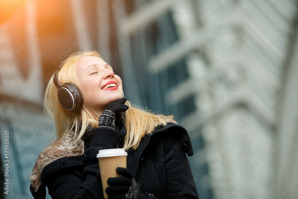Fototapeta premium Carefree beautiful young woman enjoying music and hot coffee outdoors