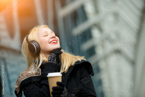 Carefree beautiful young woman enjoying music and hot coffee outdoors