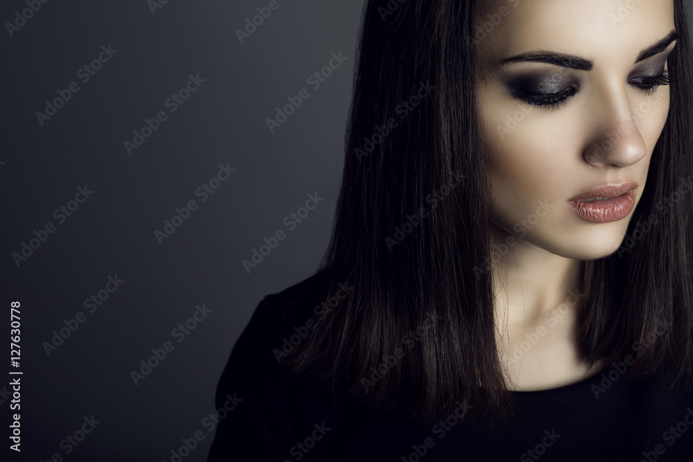 Portrait of gorgeous dark-haired woman with provocative make up looking down with sad expression on her face. Feelings and emotions concept. Close up. Studio shot. Copy-space Portrait of gorgeous dark-haired woman with provocative make up looking down with sad expression on her face. Feelings and emotions concept. Close up. Studio shot. Copy-space