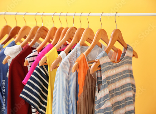 Hangers with different female clothes on yellow background