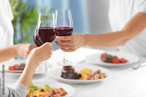 Women clinking glasses with wine and delicious dishes on table in restaurant