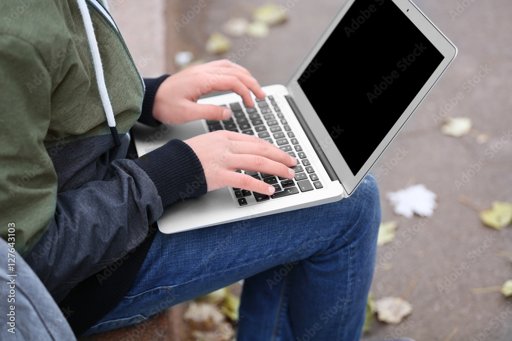 Fototapeta premium Teenager sitting on parapet with laptop in autumn day, close up