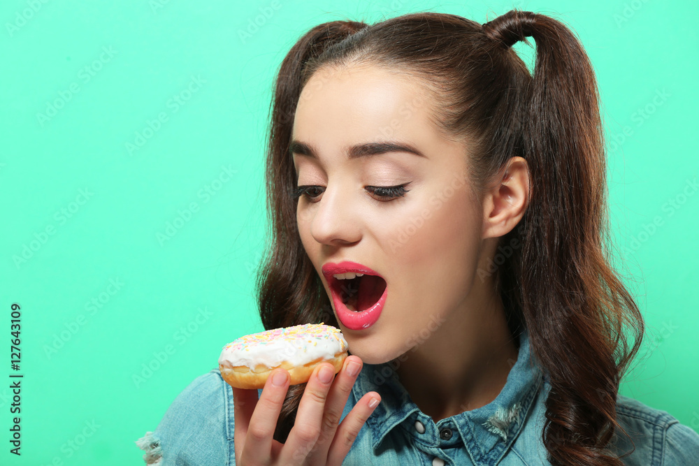 Funny young woman eating tasty donut on color background Funny young woman eating tasty donut on color background
