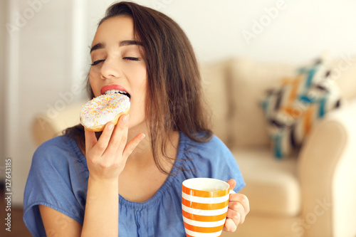 Beautiful young woman with tasty donut and cup of coffee on blurred background