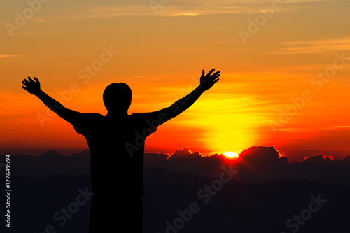 Silhouette of man with raised hands over sunset background.