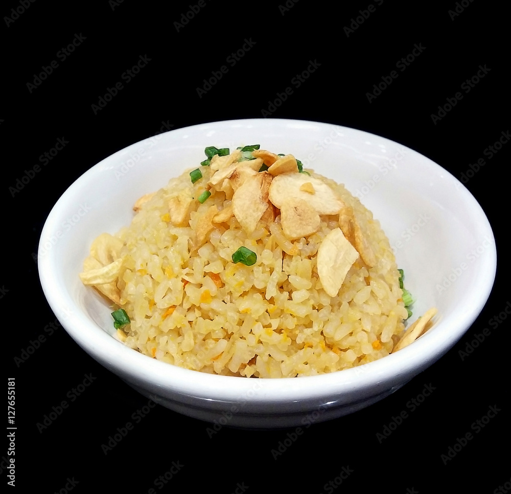 Thai garlic fried rice with vegetable on top in white bowl isolated on black background