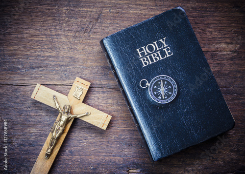 The crucifix of jesus and the compass on holy bible with on wooden background