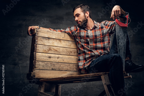 A man in a red plaid shirt, sits on a wooden box and holds hands
