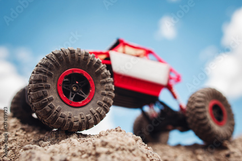 Rc crawler outside, view from below. Red and white toy suv on rocky terrain, blue sky on background, free space photo